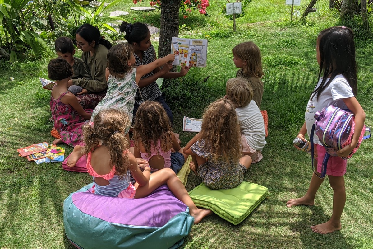 An adult reading with children seated together in a garden.