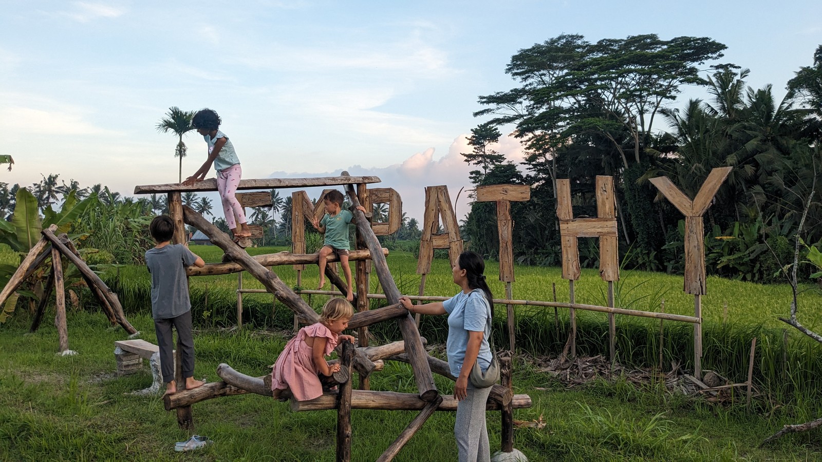 Children climb a wooden play structure beside large wooden EMPATHY letters.