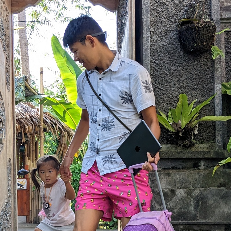 An adult and child hold hands at a school entrance.