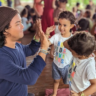 An adult and a smiling child touch raised palms while another child stands beside them.