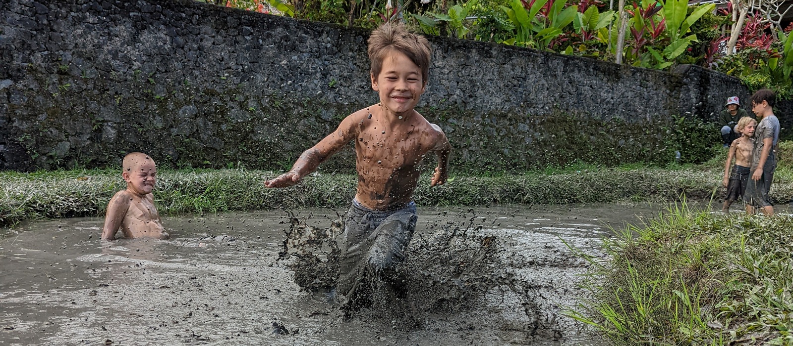 A child runs through mud while other children play nearby.