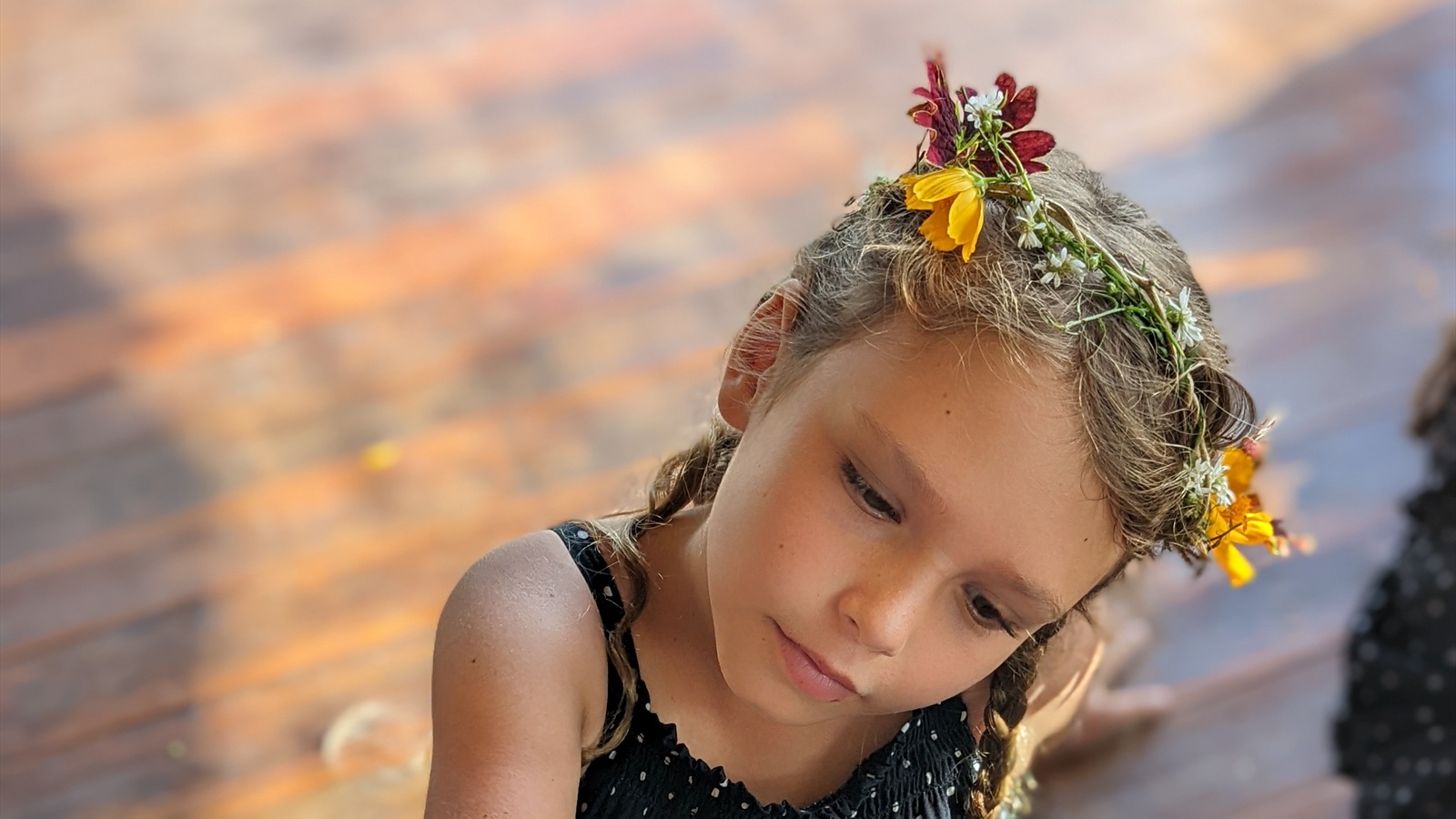 A child wearing a flower crown looks down during an activity.