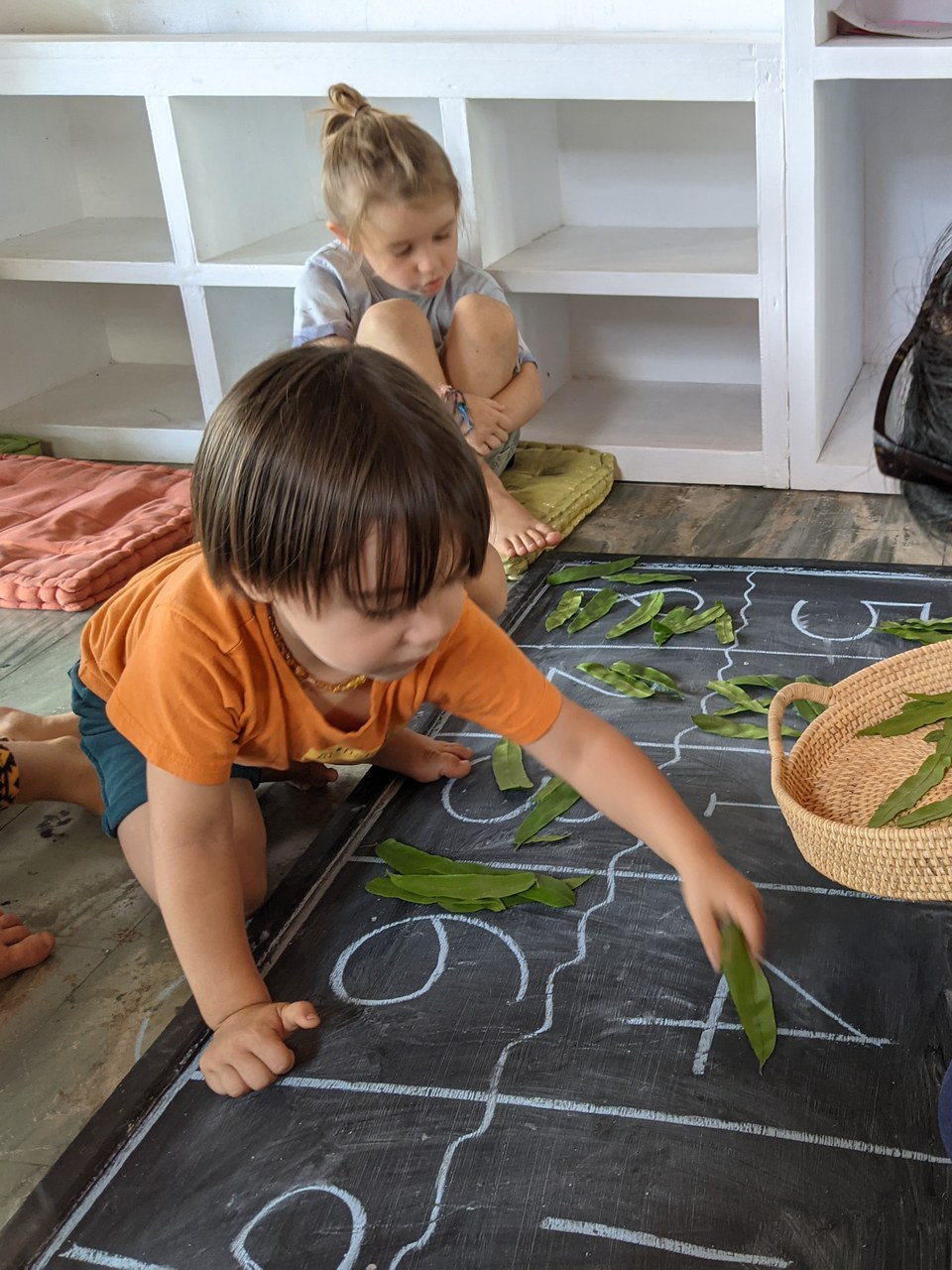 A child places leaves beside chalk numbers on a board.